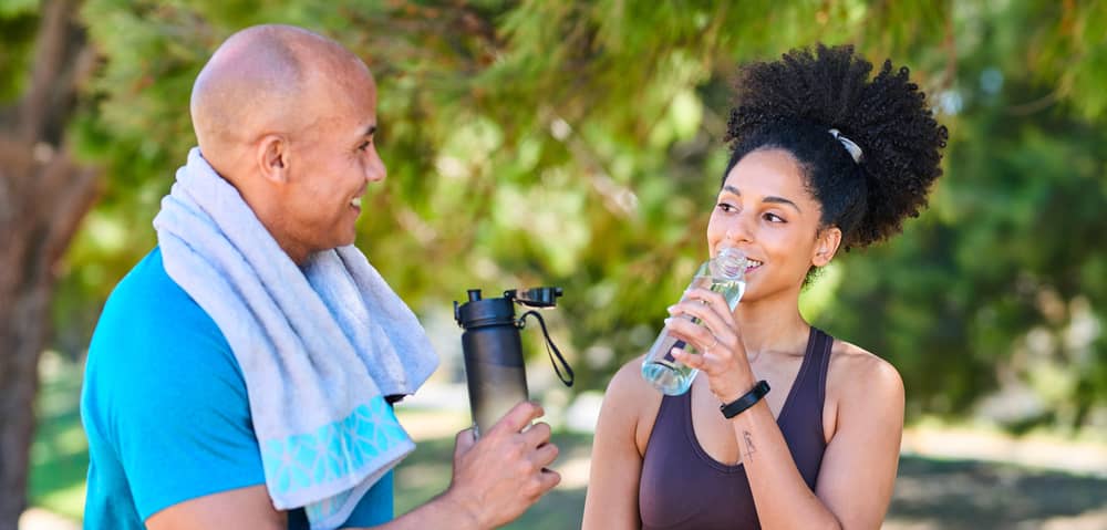 Zwei Freunde trinken Wasser nach einem Outdoor-Workout im Sommer.