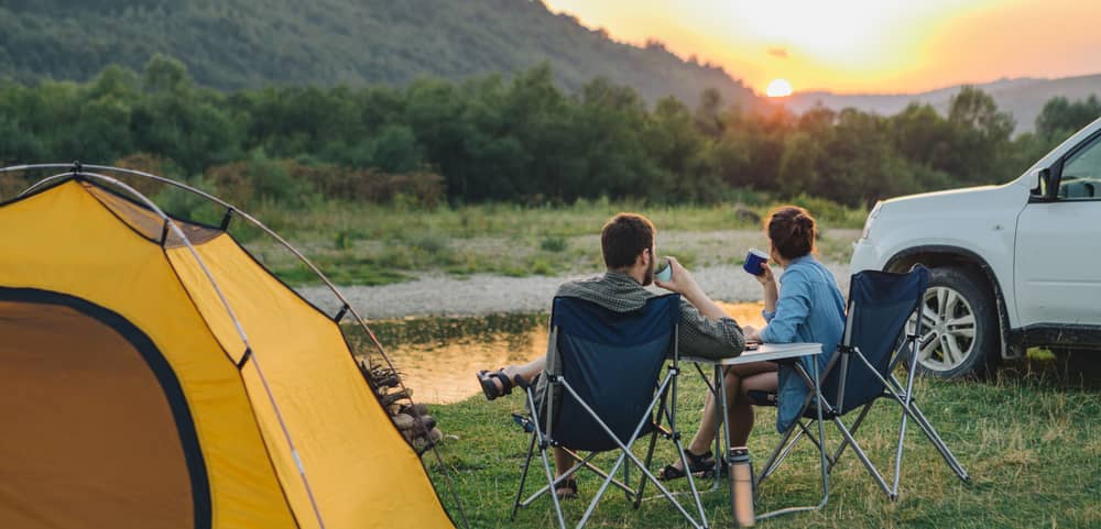 Pärchen in Campingstühlen mit Aussicht auf Sonnenuntergang in den Bergen.