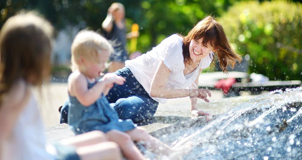 Mutter mit zwei Kindern suchen Abkühlung an einem Stadtbrunnen im Sommer.