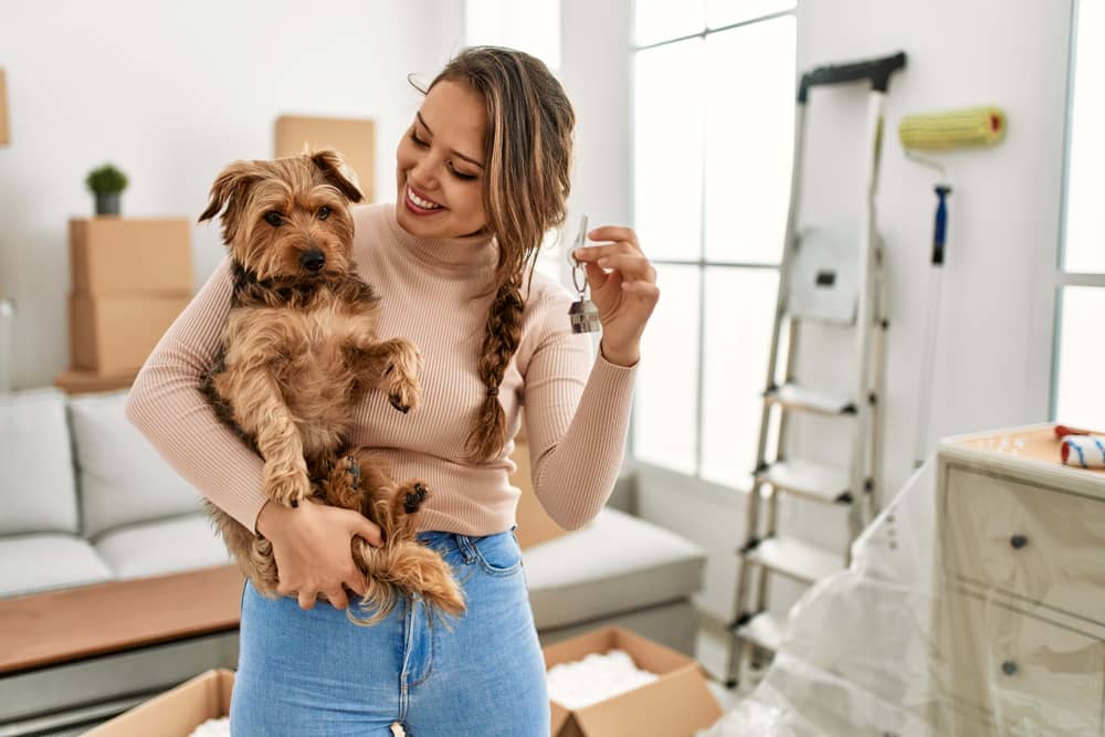 Eine junge Frau mit Hund hält einen Wohnungsschlüssel in ihrer neuen Wohnung.