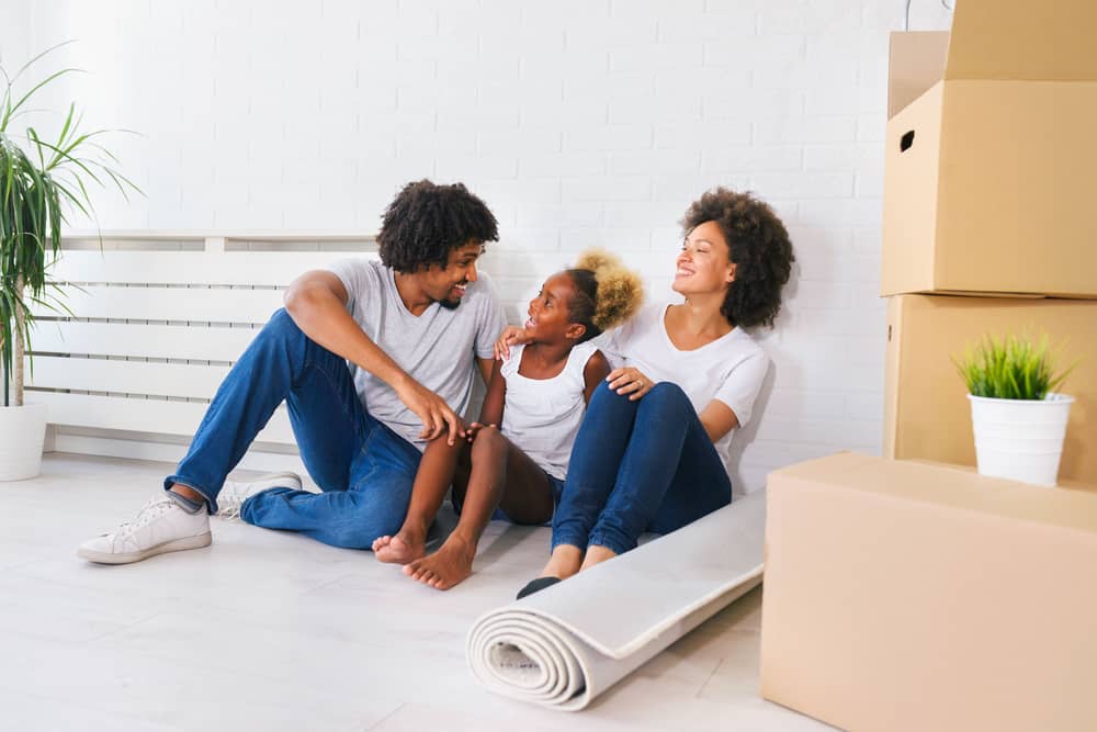 Eine junge dreiköpfige Familie sitzt neben Kartons in einer neuen Wohnung.