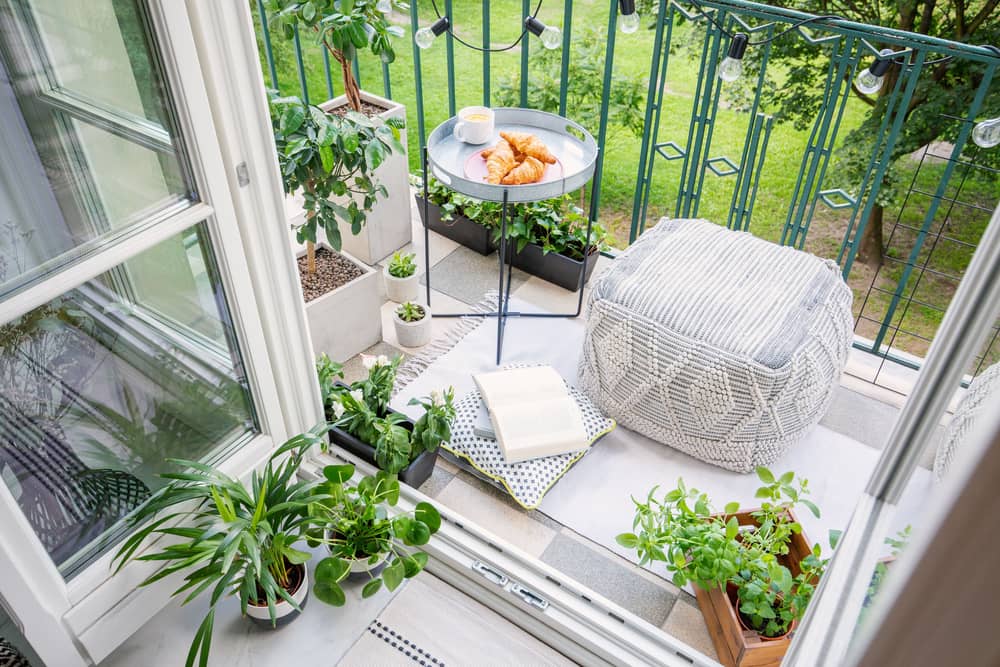 Ein kleiner Balkon mit Pflanzen, einem Sitzkissen und einem Beistelltisch mit etwas zu essen.