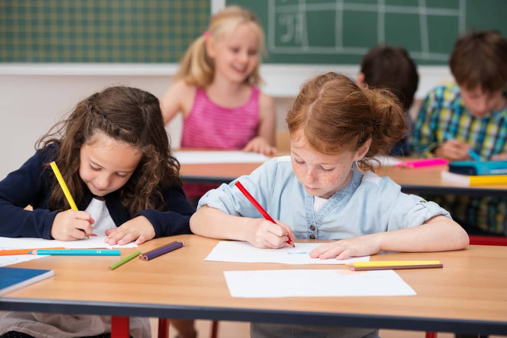 Grundschüler sitzen in einem Klassenraum und malen mit Buntstiften.