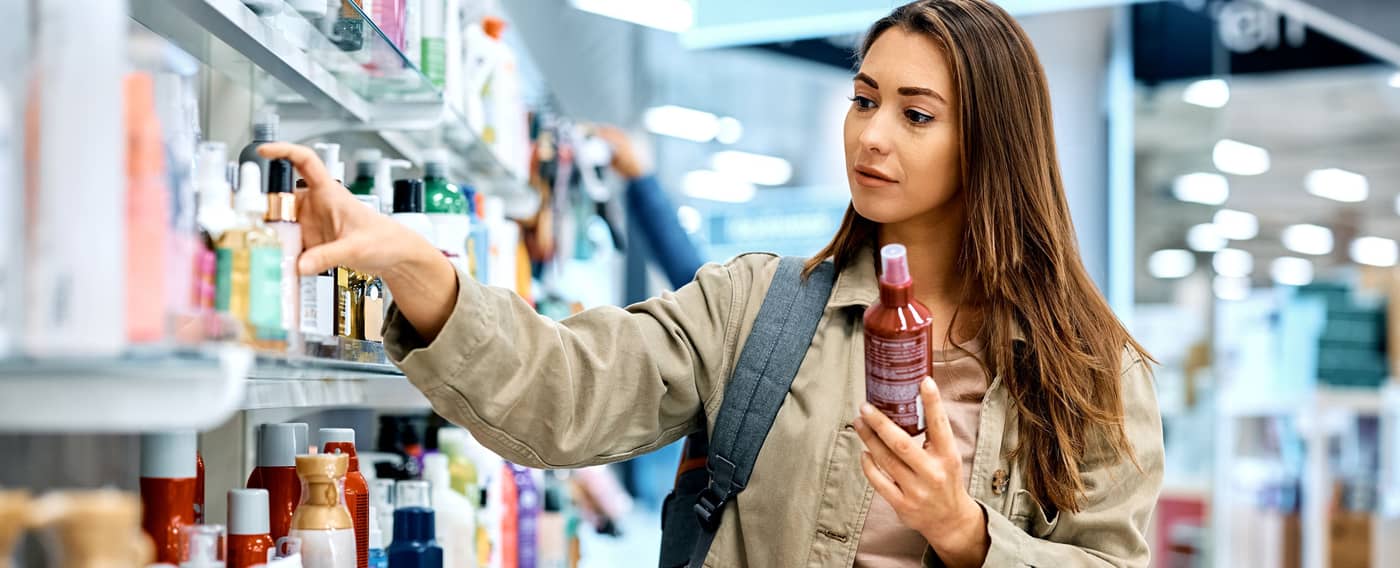 Eine Frau steht vor einem Regal in der Drogerie und studiert die Produkte