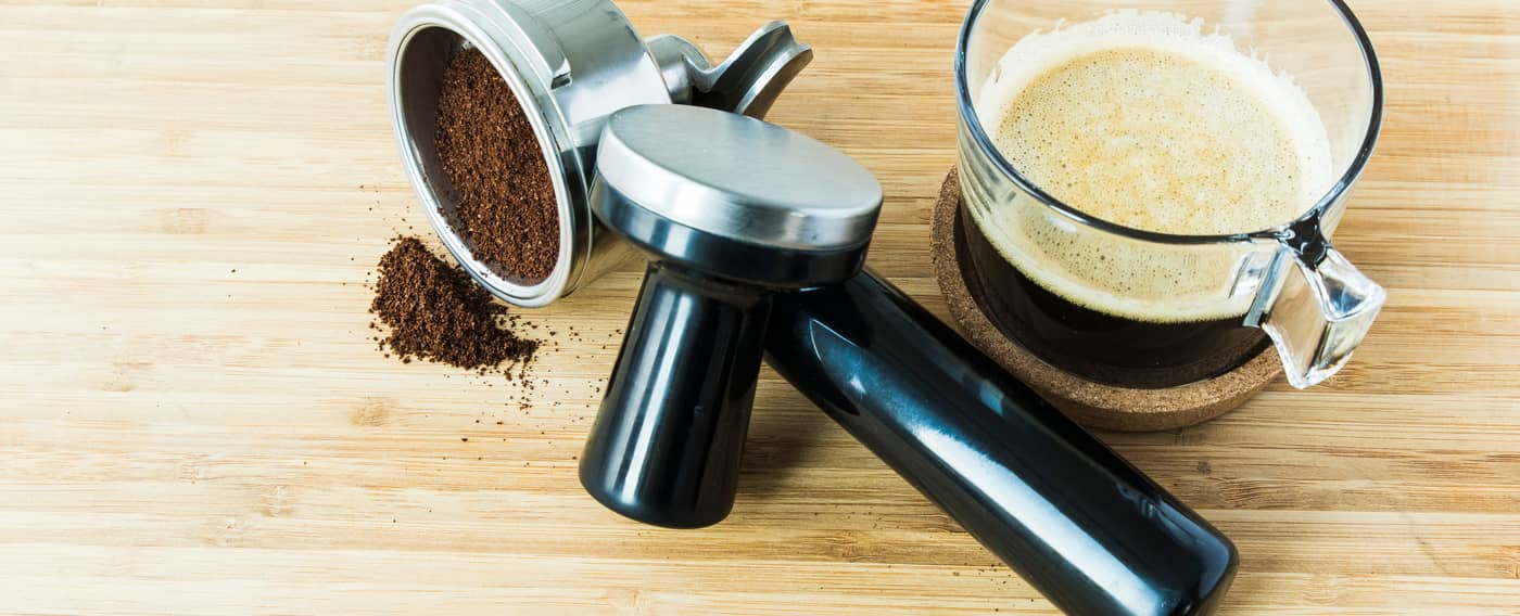 Kaffee-Siebträgereinsatz, Temper und fertige Tasse Kaffee auf einem Holztisch.