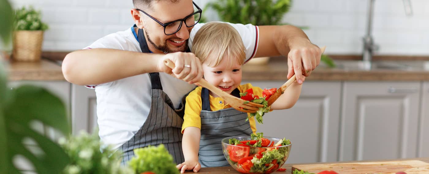 Vater und Kind sitzen vor verschiedenen Gemüsesorten und bereiten Salat zu