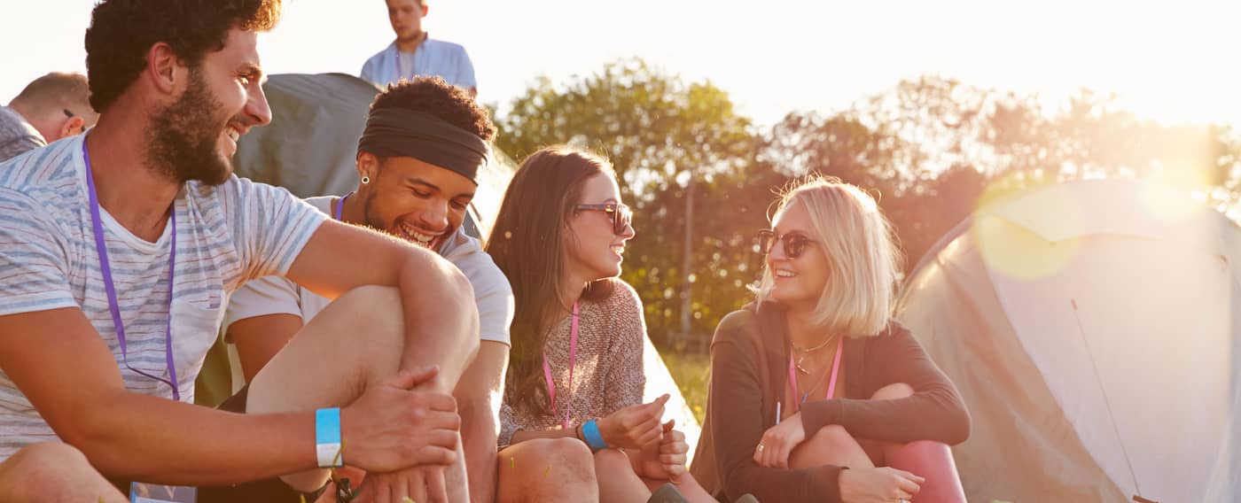 Eine Gruppe junger Leute sitzt auf einer Wiese eines Festivalgeländes