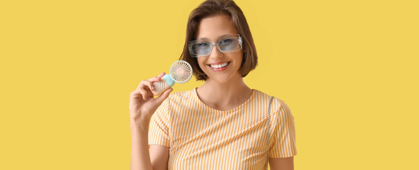 Eine Frau mit Sonnenbrille hält einen tragbaren Mini-Ventilator.