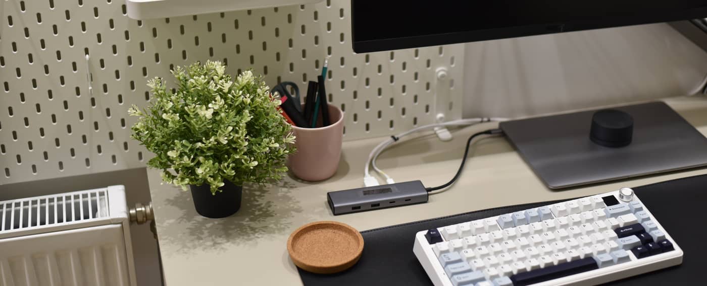 Ein Schreibtisch mit Bildschirm, Tastatur und Laptop. Alles ist ordentlich mit Kabeln verbunden. Dahinter sind kleine Gegenstände an einer Lochwand befestigt oder liegen in eingehängten Schubladen.