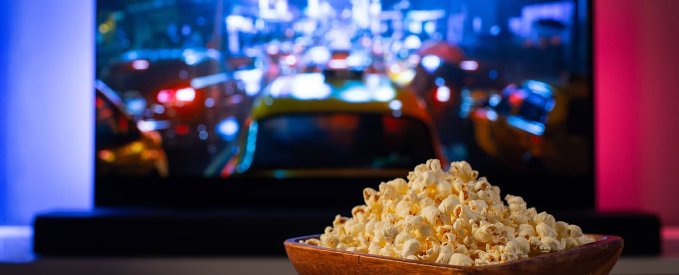 Eine Schale Popcorn und eine Fernbedienung vor einem großem Fernseher