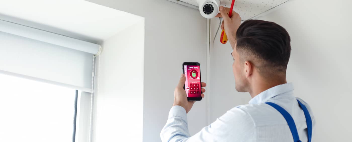 Ein Mann bringt eine Sicherheits-Kamera an und installiert auf dem Smartphone ein Alarm-System.