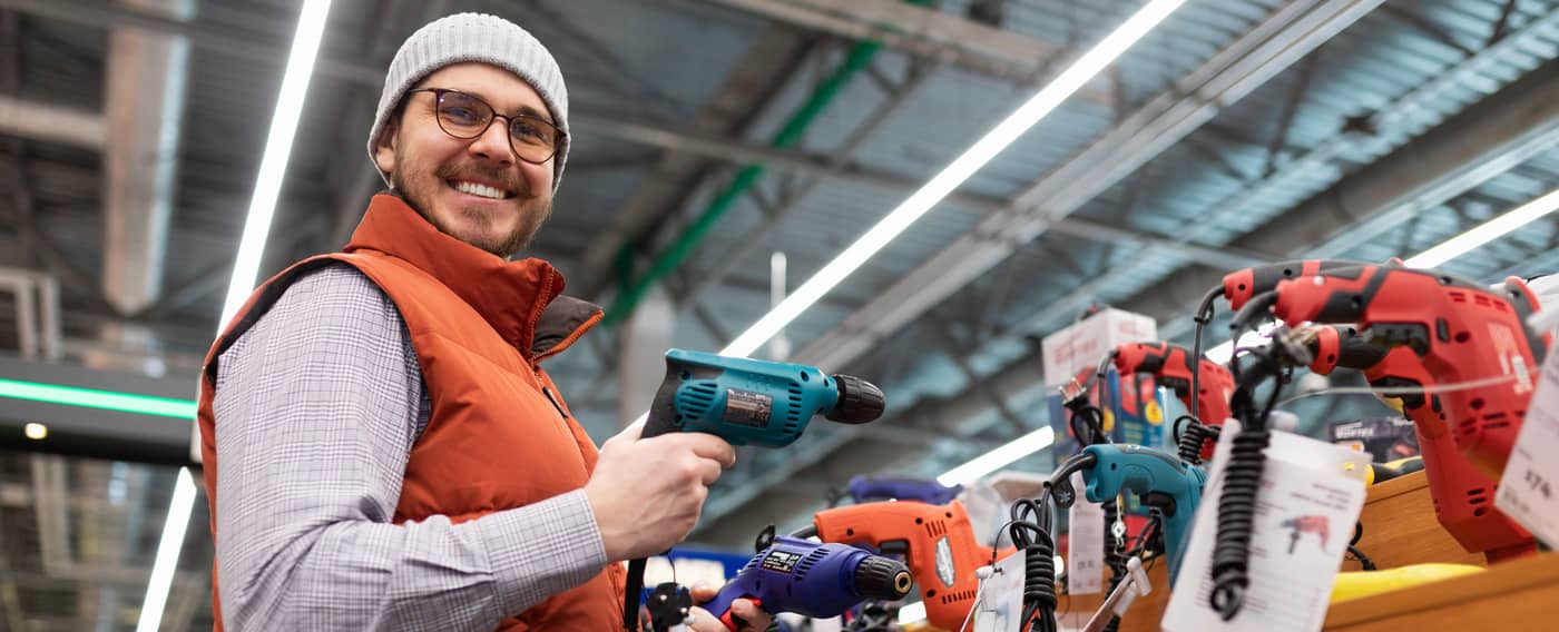 Ein Mann steht mit breitem Lächeln in einem Baumarkt und hält einen Schraubenzieher