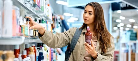 Eine Frau steht vor einem Regal in der Drogerie und studiert die Produkte