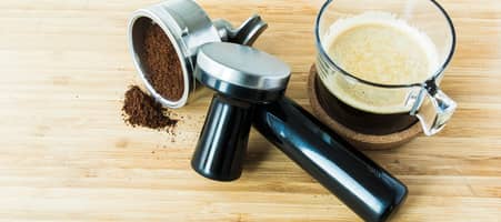 Kaffee-Siebträgereinsatz, Temper und fertige Tasse Kaffee auf einem Holztisch.