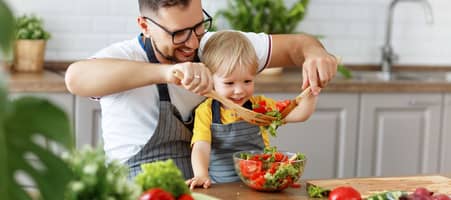 Vater und Kind sitzen vor verschiedenen Gemüsesorten und bereiten Salat zu