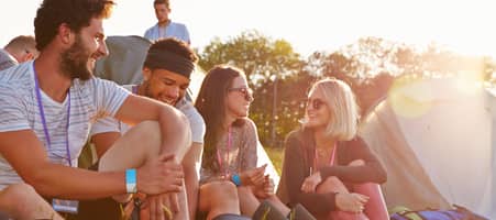 Eine Gruppe junger Leute sitzt auf einer Wiese eines Festivalgeländes