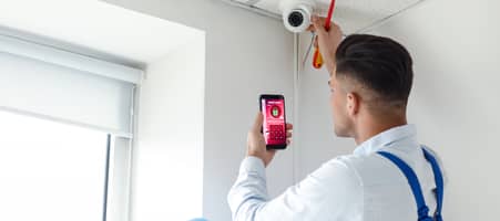 Ein Mann bringt eine Sicherheits-Kamera an und installiert auf dem Smartphone ein Alarm-System.