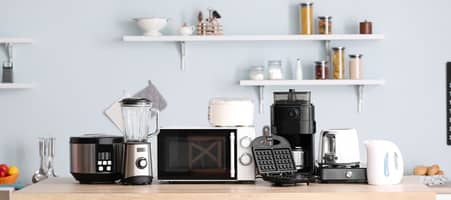 Eine moderne Küche mit vielen Küchengeräten wie einem Toaster, einem Smoothie-Maker und einem Waffeleisen auf der Arbeitsplatte.